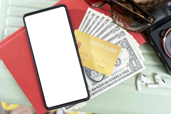 Smartphone with blank screen, credit card, and pile of money are placed on a table. The credit card is a Visa card. The pile of money is made up of several different denominations of US currency.