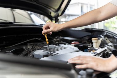 Close-up photo of woman's hand check engine oil A woman pulls out the dipstick to check the oil level of her car. Woman repairing car in garage or workshop Work and repairs at home.