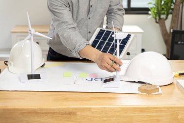 Desk of architects Solar Energy Powered Home Green for reduce global warming concept. Young businessman with wind turbine and solar panels at desk in office.