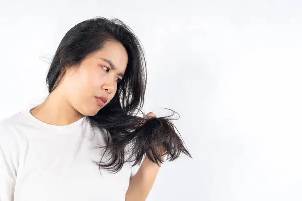 A woman with long hair is looking at the camera. She has just cut her hair and is holding it up. Sad young woman holding her long hair split ends in hand and touching chin isolated white background.