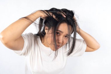 Kuru kafa derisi kaşındırıyor ve kepekli uzun saç. Uzun saçlı bir kadın beyaz bir arka planın önünde duruyor. Kameraya ciddi bir ifadeyle bakıyor..