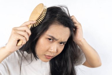 Uzun saçlı bir kadın ahşap bir fırçayla saçını tarıyor. Mutsuz görünüyor ve kaşlarını çatıyor..