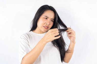 Bir kadın saçını makasla kesiyor. Mutsuz görünüyor ve elinde makası tutuyor.