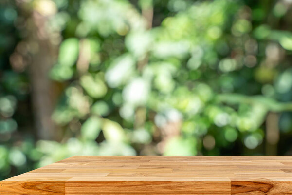 A wooden table with a view of trees in the background. The table is empty and has a natural, rustic feel to it. Concept of calm and tranquility, as if one were sitting at the table.