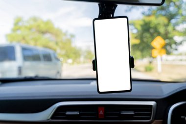 Ön camında manzaralı bir yol olan gösterge panelinde beyaz ekran akıllı telefon. Arabanın ön camında boş ekran olan akıllı telefon. Reklam tasarımınız için boş ekran.