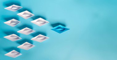 Mavi arka planda kağıt tekneler olan liderlik kavramı. Bir lider gemi diğer gemilere liderlik ediyor. Filtrelenmiş ve tonlanmış görüntü. Renkli origami gemileri..