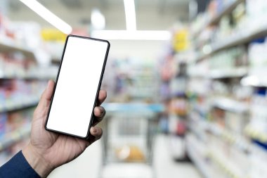 Markette alışveriş yaparken arka planda ürün reyonu olan akıllı telefonu tutan bir kadının kişisel perspektifi. Tasarım modeli için boş ekranlı akıllı telefon