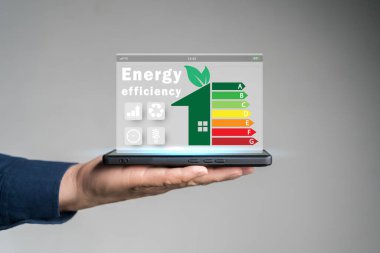 Enerji verimliliği kavramı. Enerji verimli ev inşa hızı denetimi için sanal ekranda enerji verimliliği derecelendirme simgesine sahip tablet kullanan kişi. Yenilenebilir enerji kavramı.