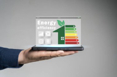 Enerji verimliliği kavramı. Enerji verimli ev inşa hızı denetimi için sanal ekranda enerji verimliliği derecelendirme simgesine sahip tablet kullanan kişi. Yenilenebilir enerji kavramı.