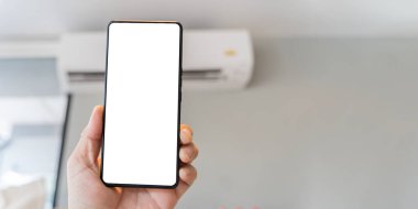Bir erkek teknisyen elinde boş beyaz ekran maketi kullanarak cep telefonu tutuyor. Klimayı telefonla kontrol etmek akıllıca. Kesme yolu.