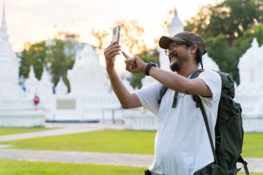 Mutlu blog yazarı Kafkasyalı, erkek, etkileyici blog yazarı, neşeli gülümseyen turist sosyal medya kanalı rekor blog seyahati. Seyahat sırasında görüntülü arama yaparken cep telefonu kullanan mutlu turist