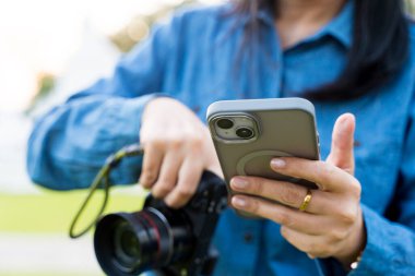 Fotoğrafçı evde telefon ve kameraları kontrol ediyor. Kişi mikrofonu özel bir sapla tutar ve diğer eliyle objeyi görmek için görüntü ayarlar.