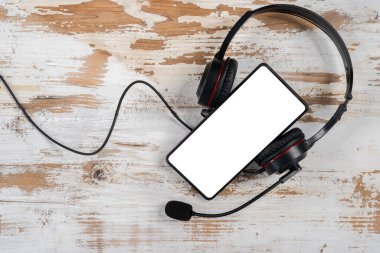Boş akıllı telefon ekranı ve kulaklıklar, modern cep telefonu eğlence ve podcast teknolojisi, bir masaya yerleştirildi. Parh kırpılıyor.