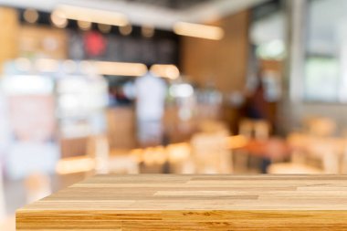 Tahta masa bulanık arkaplanın önünde boş. Kahverengi ahşap, bulanık kahve dükkanında. Ürünlerinizi görüntülemek veya montajlamak için kullanılabilir. Ürünün gösterimi için modelle.