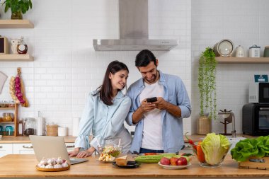 Evde akıllı telefon ve laptop kullanan neşeli genç bir çiftin portresi. Çift karı koca yeni bir dizüstü bilgisayarda yazı yazıyorlar sohbet blogları paylaşıyorlar.