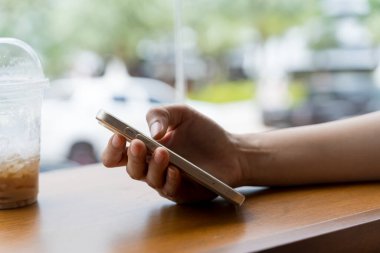 Kahve dükkanında ahşap masada akıllı telefon kullanan Asyalı kadının eli. Kafe 'de elinde kahve fincanı olan akıllı bir telefon tutan ve kullanan bir adamın yakın plan görüntüsü.