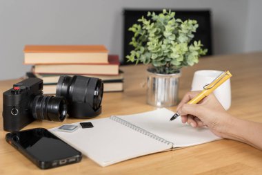 Defterine yazan biri. Seyahat günlüğü pasaport cüzdanı, kamera kamerası, akıllı telefon ve saat gibi gezici eşyalarla çevrilidir.