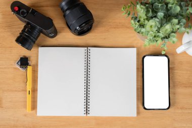 Akıllı telefonu ve kameraları olan bir fotoğrafçı masası. Tasarımcı günlük malzemeler. Boş spiral defter ve kalemle eski bir kamera..