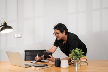 Adam dizüstü bilgisayardaki fotoğrafları düzenliyor, grafiksel tablet ve interaktif kalem ekranı kullanıyor, kafedeki masada bir fincan çayla oturuyor. Web tasarımcısı proje, fotoğraf işleme üzerinde çalışıyor.