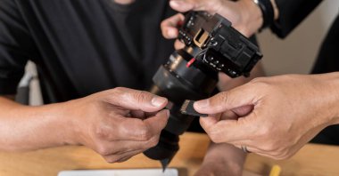 Ofiste çalışırken DSLR kamera. Stüdyolarındaki fotoğrafçılar. Olgun profesyonel fotoğrafçı evde çalışıyor. Erkek fotoğrafçı profesyonel fotoğrafçısına hafıza kartı takmaya hazır. 