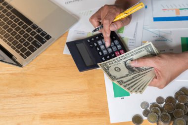 Yakından bakınca iş adamı bankacı para banknotları, banka finans ve yatırım kavramlarını sayıyor. İş adamı hesap makinesi kullanıyor, para sayıyor ve gelir ve giderleri planlıyor.