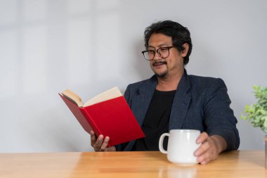 Olgun bir adam pencere kenarından kitap okuyor, gözlük takıyor, fotokopi çekiyor. Yetişkin erkek işadamı evde kitap okuyor. Genç adam evde kitap okuyor..
