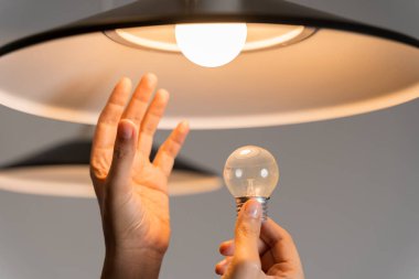 Ampulü değiştiriyorum. Adam yeni evine lamba döşemiş. Bir adam tek başına bir dairede ampul değiştiriyor. Erkek eller parlak bir ampulle LED lambayı karşılaştırır..