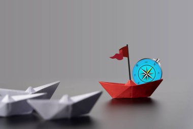 Beyaz teknelerle çevrili pusula gülüne tünemiş kırmızı kağıt tekne yön ve liderliği sembolize ediyor. Pusula üzerindeki kırmızı kağıt tekne, küçük beyaz teknelerden oluşan bir filoya önderlik ediyor. İş Liderliği