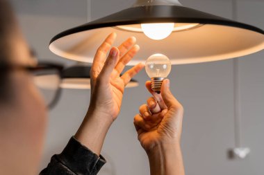 Erkek eller parlak bir ampulle LED lambayı karşılaştırır. Ampulü değiştiriyorum. Adam yeni evine lamba döşemiş. Bir adam tek başına bir dairede ampul değiştiriyor..