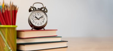 Kitapların yanında eski altın çalar saat ve beyaz arka plandaki ahşap bir masada renkli kalemler. Son teslim tarihi. İyi sabahlar. Okulda ve üniversitede öğrenim.