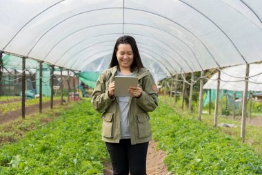 Akıllı çiftlik. Tarlada tableti olan genç bir kadın çiftçi. Tarım, bahçıvanlık, iş ya da ekoloji konsepti. Büyüme dinamikleri. Bir çiftlikte çalışırken dijital tablet kullanan bir kadın.