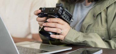 Bir kadın kamerayı tutuyor ve üzerinde resimler olan tablete bakıyor. DSLR fotoğraf makinesindeki fotoğrafları dizüstü bilgisayara aktaran kadın. Kafede çalışan genç kadın fotoğrafçı, serbest çalışan..