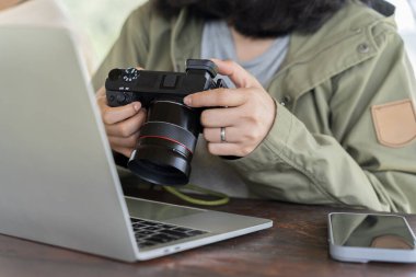 Bir kadın kamerayı tutuyor ve üzerinde resimler olan tablete bakıyor. DSLR fotoğraf makinesindeki fotoğrafları dizüstü bilgisayara aktaran kadın. Kafede çalışan genç kadın fotoğrafçı, serbest çalışan..