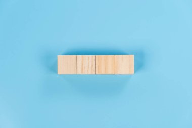 Mavi arka planda düz bir çizgide sıralanmış dört tahta blok temel, hizalama ve dengeyi sembolize ediyor. Eğitim, planlama veya iş fikri için asgari ve temiz bir kavram.