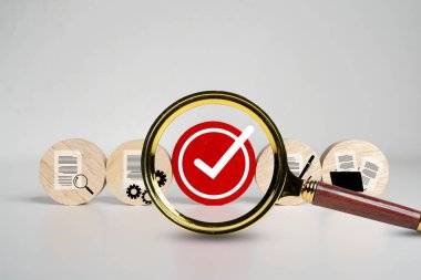 Belge simgeleriyle çevrili kırmızı bir onay işaretini vurgulayan büyüteç, kalite güvencesini, onay sürecini, doğrulama, denetim, uygunluk, onaylama ve belge gözden geçirmesini sembolize ediyor.