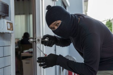 Maskeli hırsız bir eve girmek için tornavida kullanıyor. Şehir ortamlarında haneye tecavüz, hırsızlık, hırsızlık, suç önleme ve konut güvenliği tehdidi kavramı.