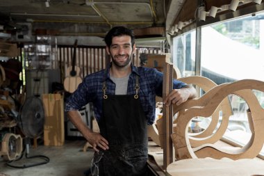 Ahşap gitar çerçeveleriyle çevrili bir atölyede gururla duran güler yüzlü Luthier 'in portresi. Flanel gömlek ve önlük giyiyor, işçiliğine güveniyor. El yapımı enstrüman ve tutku kavramı.