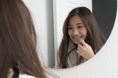 Banyodaki aynadaki yansımasına gülümseyen uzun saçlı mutlu genç kadın diş tellerini gösteriyor. Ortodontik tedavi, diş bakımı, özgüven ve sağlıklı bir gülümseme kavramı..