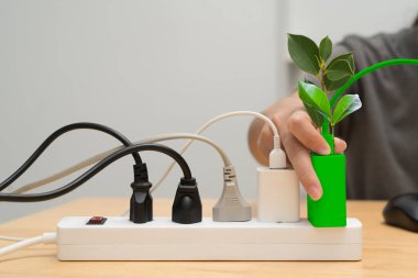 Yeşil bir cihazın kablolarla dolu bir güç şeridine bağlanması, sürdürülebilir ve çevre dostu bir dünya için yeşil enerjiyi, temiz enerjiyi, enerji tasarrufu ve çevresel bakımı sembolize ediyor..