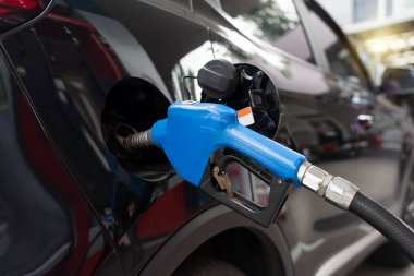 Bir benzin istasyonunda siyah bir arabaya benzin pompalayan mavi bir yakıt hortumunun yakın çekimi. Modern kentsel yaşamda ulaşım enerjisi, yakıt ikmali, benzin maliyeti ve otomobil bakımı kavramı.