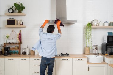 Modern bir evin içinde mutfak kaputunu bezle temizleyen eldiven giyen bir adam hijyen, temizlik, sorumluluk, ev işi, bakım ve sağlıklı yaşam tarzını sembolize ediyor..