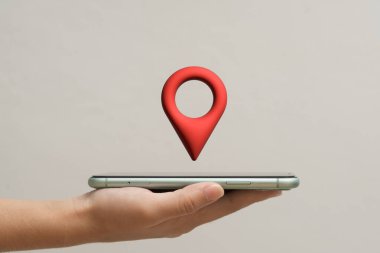 Yukarıda yüzen kırmızı konum simgesi olan akıllı telefonu tutan bir insan eli, GPS, navigasyon, harita, seyahat, yön, çevrimiçi hizmet, teknoloji, izleme ve dijital iletişimi sembolize eder..