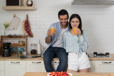 Modern mutfakta taze portakal suyunun tadını çıkaran genç bir çift, gündelik yaşam tarzı, aşk ve ilişki, neşeli bir sabah birlikte, sağlıklı içki, pozitif ruh hali, mutluluk ve kapalı alanlarda kaynaşma.