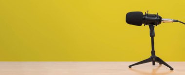 Podcast, müzik kaydı, yayıncılık, stüdyo, ses iletişimi ve dijital içerik oluşturma kavramı için uygun sarı arkaplan tripodunda profesyonel siyah mikrofona yakın çekim.