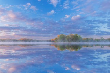 Güneşin doğuşuyla Whitford Gölü kıyılarının sisli bahar manzarası sakin sulardaki yansımalarla, Fort Custer State Park, Michigan, ABD