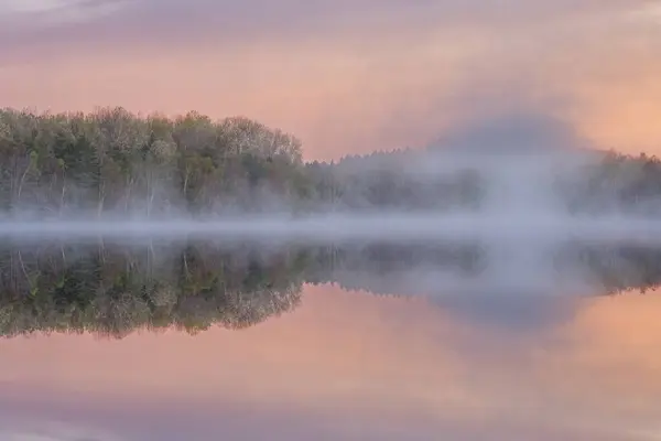 モカシン湖の夜明けの霧のような春の風景 穏やかな水の中の鏡のような反射 ヒワタナショナルフォレスト ミシガン州のアッパー半島 ストックフォト