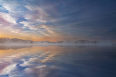 Spring landscape at dawn of the shoreline of Whitford Lake, with mirrored reflections in calm water, Fort Custer State Park, Michigan, USA