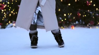 Çizmeli kadın bacakları hareket ediyor ve Noel ağacının yanında karda dans ederken adımlar atıyor. Mutlu yıllar.