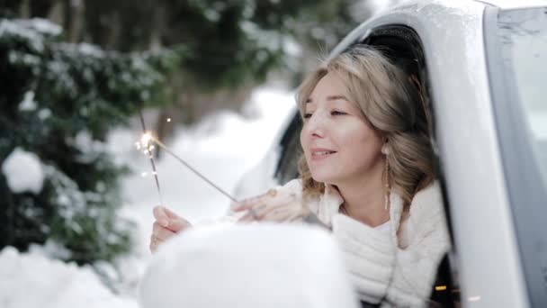 魅力的な幸せな若い女性が車の窓の外に傾いて火花を保持する 冬の旅行 週末のレクリエーション 明けましておめでとうございます — ストック動画