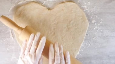 Yemek masasında merdane kullanarak kalp şeklinde pizza yapıyorlar. Yüksek açı görünümü